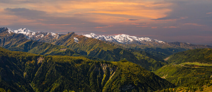 Panoramic landscape photograph of majestic snow capped mountain range stretching under sunset sky in Svaneti Georgia.