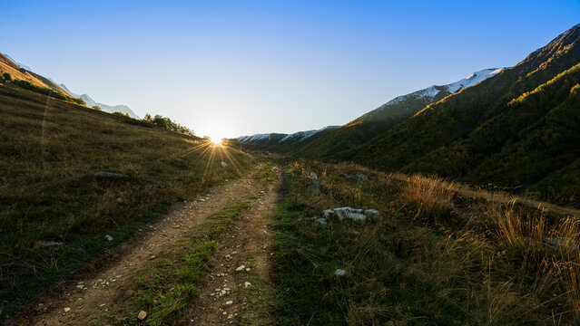 Dirt trail path winding through mountain valley towards rising sun in Adishi, Svaneti region, Georgia. Trekking and travel background.