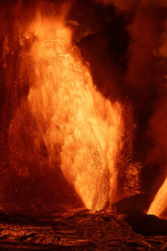 View of the Kilauea Crater erupting with a powerful fountain of molten lava and glowing volcanic debris against the dark night sky in Hawaii County, Hawaii, United States.