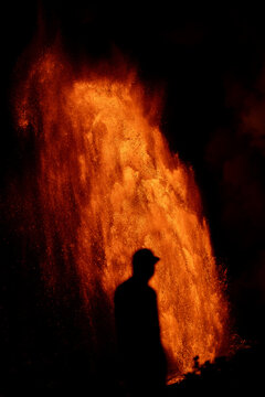View of the silhouette of a person standing before a massive glowing lava fountain at Kilauea Crater in Hawaii County, Hawaii, United States.