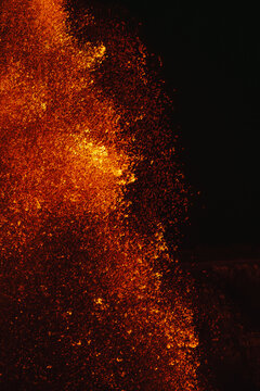 View of Kilauea Crater erupting with glowing molten lava and sparks against a dark night sky in Hawaii County, Hawaii, United States.