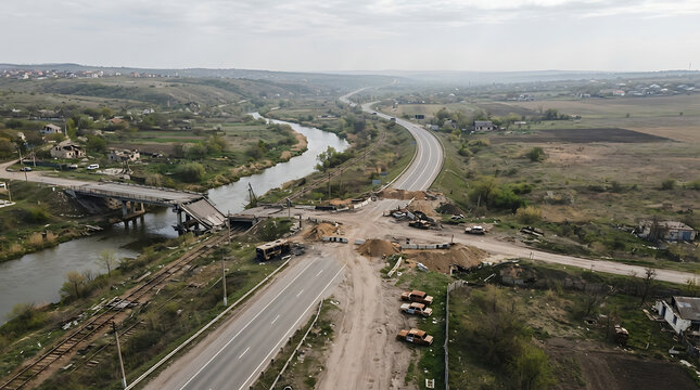 Aerial view of a destroyed bridge and temporary road crossing over a river in a rural landscape after conflict