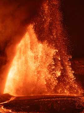 View of Kilauea Crater erupting with intense glowing lava fountains and molten rock spraying into the night sky in Hawaii County, Hawaii, United States.