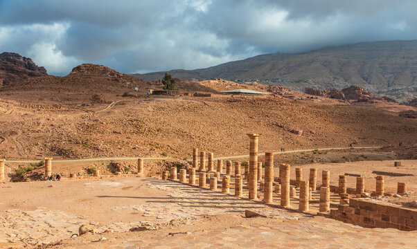 View of the Great Temple in Petra with ancient stone columns, rocky desert landscape, and cloudy sky in Wadi Musa, Ma'an Governorate, Jordan.