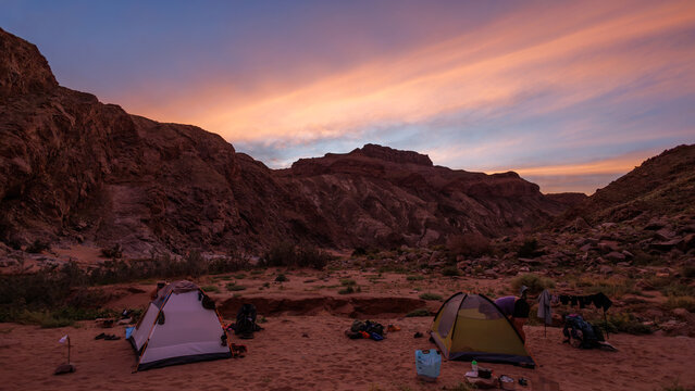 View of tents pitched on the sandy floor of Fish River Canyon at sunset with dramatic rocky cliffs under a colorful sky in Hobas, Karas Region, Namibia.