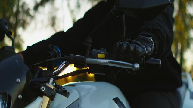 Close-up cinematic sequence of a motorcyclist gripping handlebars and riding a modern street bike with bright headlight through a scenic forest road at sunset