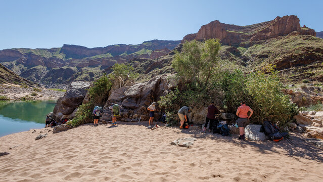 View of hikers resting on the sandy banks of the Fish River in Fish River Canyon, surrounded by rugged cliffs and desert landscape in Hobas, Karas Region, Namibia.