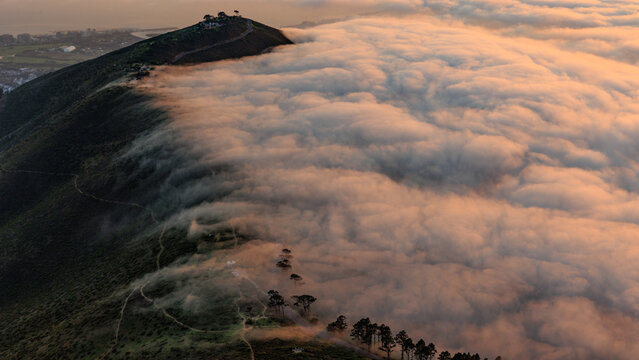 View of Lion's Head peak rising above a thick blanket of clouds during golden hour in Cape Town, Western Cape, South Africa.