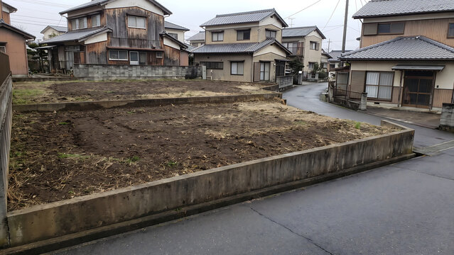 擁壁の上に二段の土が見える住宅地の空き地と戸建て住宅、生活道路に面する土地の景観