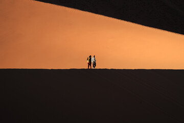 Fototapeta premium Two hikers dwarfed by the slope of a giant dune