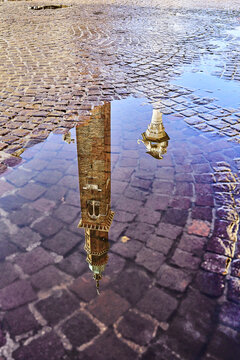 View of the reflection of the historic Torre Bissara bell tower in a puddle on the cobblestone pavement of Piazza dei Signori in Vicenza, Veneto, Italy.