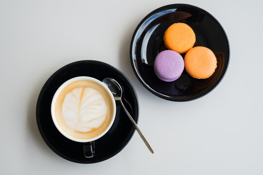 Cappuccino cup with latte art and colorful French macarons on black saucers for coffee shop menu concept