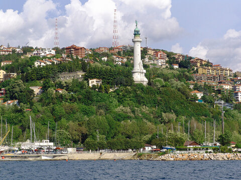 View of the Victory Lighthouse standing on a lush green hillside overlooking the harbor with residential buildings and radio towers in the background in Trieste, Friuli-Venezia Giulia, Italy.