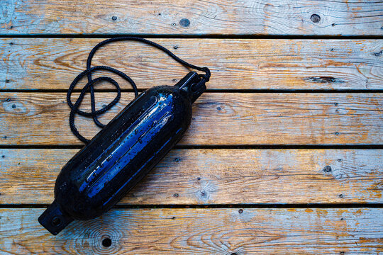Black cylindrical boat fender rests on a weathered and wet wooden dock.