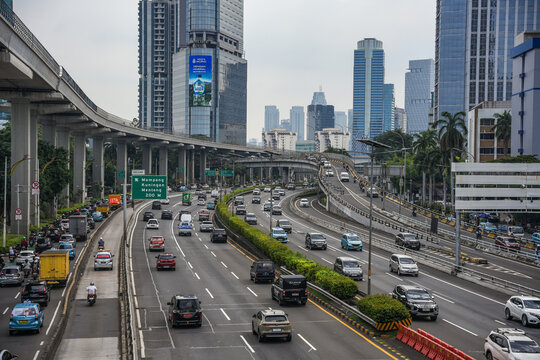 View of busy multi-lane highway traffic flowing beneath an elevated road structure with modern skyscrapers and urban architecture in the background in Jakarta, Jakarta, Indonesia.