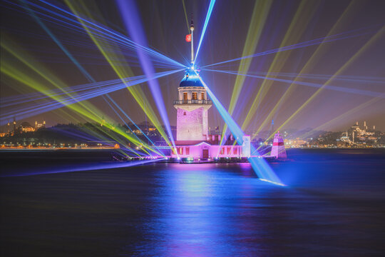 View of the illuminated Maiden's Tower at night featuring a vibrant laser light show with blue and yellow beams reflecting on the Bosphorus waters in Istanbul, Istanbul, Turkiye.