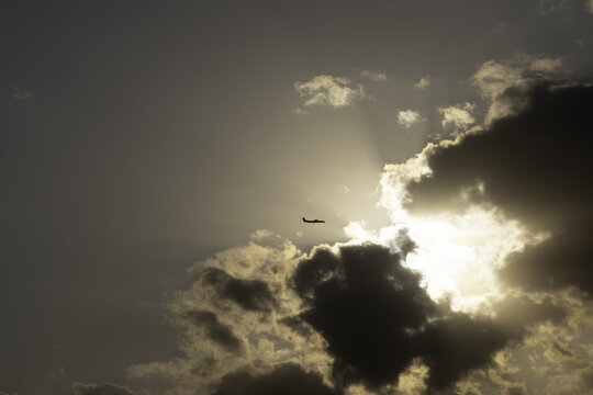 View of a small airplane silhouetted against the bright sun and dramatic clouds over the landscape of Nairobi National Park in Nairobi, Nairobi County, Kenya.