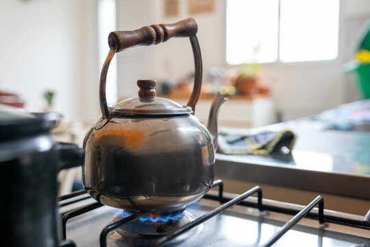 Vintage metal kettle heating water over gas stove flame in home kitchen