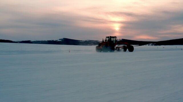 Motor Grader Working Through Powder Snow at Sunset