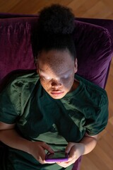 Fototapeta premium Young woman with freckles lying on a purple sofa using a smartphone illuminated by screen light in a relaxed indoor lifestyle portrait