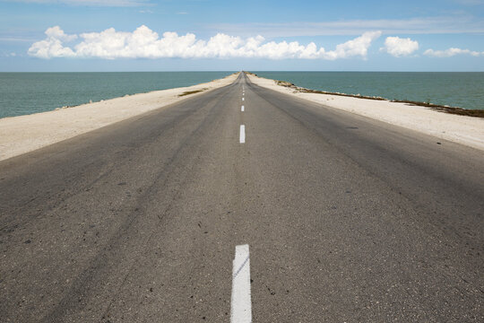 View of a long asphalt causeway stretching across the sea under a bright blue sky with scattered white clouds in Cayo Coco, Ciego de Avila, Cuba.