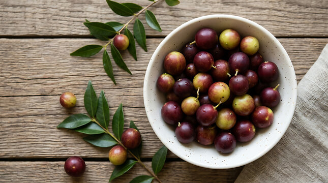 Fresh jaboticaba berries in a white bowl on a rustic wooden table with jaboticaba branches vitamins nutrition ingredient culinary vegetarian overhead