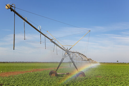 View of a center pivot irrigation system spraying water over a lush green field with a small rainbow visible in the mist under a clear blue sky in Cienfuegos, Cienfuegos, Cuba.