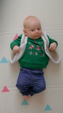 Smiling three month old baby in christmas outfit on floor rug. Slow motion. Vertical video.