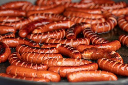 A large batch of grilled sausages with scored cuts cooking in a pan