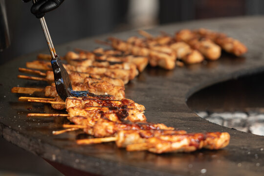 Preparing chicken meat skewers, grilled or roasted on a round griddle or a circular grill in a street food market