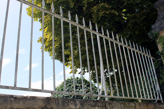Grille de cl&ocirc;ture barreaud&eacute;e en m&eacute;tal blanc avec pointes de lance sur muret en pierre