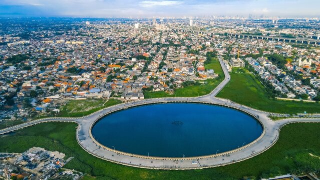 Aerial view of a large circular reservoir surrounded by dense urban housing and road infrastructure in Bekasi Barat, West Java, Indonesia.