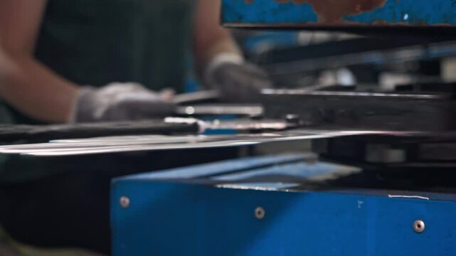 Close view isolates knitted glove traveling through machinery while operator manages surrounding production stages. Scene illustrates human machine interaction within continuous textile manufacturing