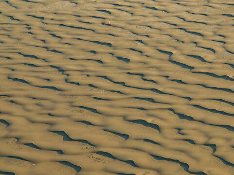 Aerial view of the sand dunes at Stokksnes with two people walking across the rippled landscape in Iceland.