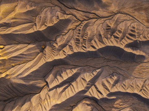 Aerial view of the eroded landscape of Caineville Mesa, featuring intricate ridges, deep gullies, and textured desert terrain under warm light in Wayne County, Utah, United States.
