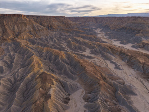 Aerial view of Caineville Mesa featuring rugged badlands, eroded clay hills, and deep gullies under a soft sunset sky in Wayne County, Utah, United States.
