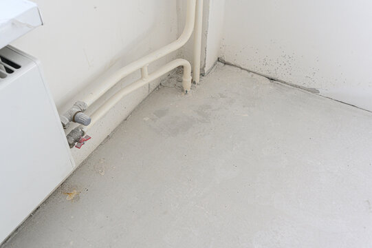 White PPR pipes along base, gray fittings, red valve, concrete floor, plain walls, utility corner, plumbing connection, minimal finish