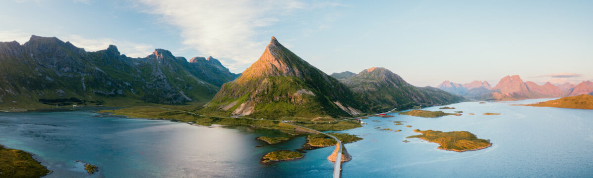 Aerial view of the dramatic peaks of Lofoten islands connected by a bridge over turquoise waters in the golden hour light in Nordland, Norway.