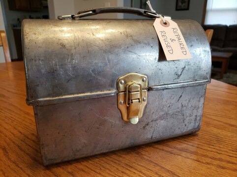 durable object showing tasteful signs of age and repair Vintage metal lunchbox with a "Fresh Feed Refused" tag on a wooden table