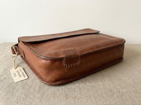 durable object showing tasteful signs of age and repair Vintage brown leather satchel with visible stitching and a price tag