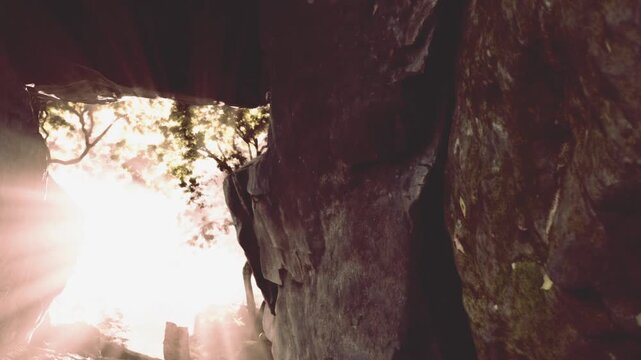 Warm sunlight streams through the rocky entrance of a cave, illuminating the stone walls. Outside, trees gently sway, adding a touch of natures beauty to the serene scene.