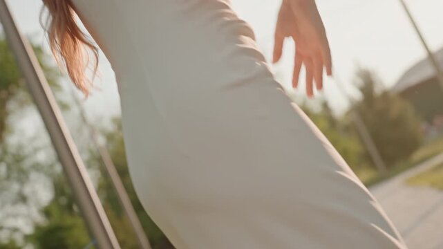 Young woman with long hair wears large headphones and white top moving through outdoor setting. scene features soft natural light string lights in background greenery visible beyond focus