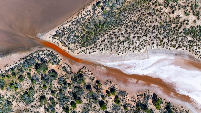 Aerial view of the salt lake landscape with reddish water, white salt deposits, and surrounding native scrubland in Wongan Hills, Western Australia, Australia.