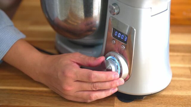 Hand Adjusting Speed Dial on Stand Mixer for Cookie Dough Preparation on Wooden Countertop