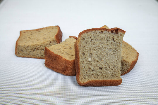 Dry stale pieces of bread lie on a textured white cloth. Golden crusts contrast with the soft, porous interior.
