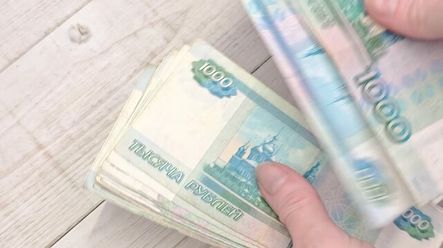 Hand counts a stack of thousand ruble banknotes, cash counting scene, financial transaction detail.