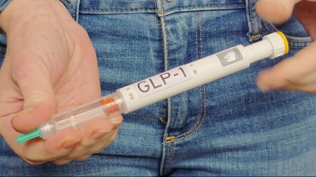 Woman adjusts the dosage on a GLP-1 injection pen wearing denim jeans, diabetes medication routine, weight management healthcare scene.