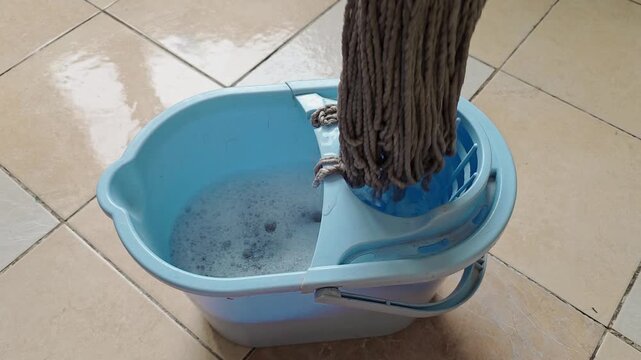Mop is wrung out in the special compartment of a cleaning bucket, household cleaning routine, floor maintenance scene.