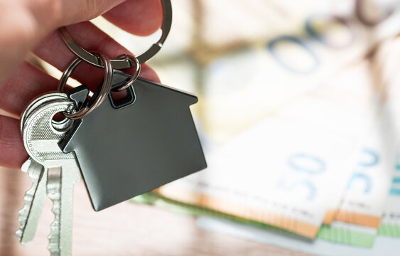 Hand holding house keys with money background