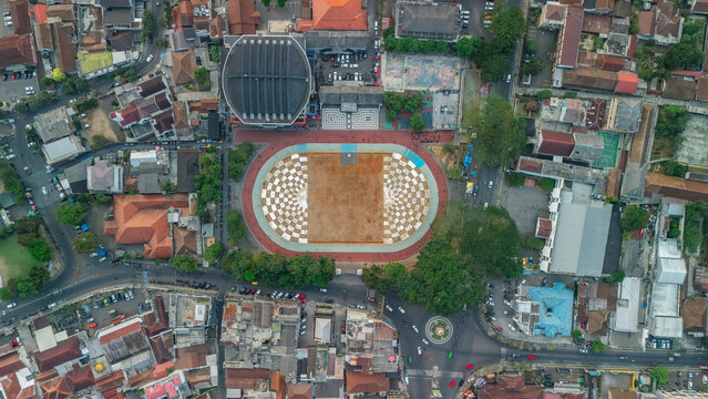 Aerial view of a town square featuring a distinctive checkered pattern surrounded by urban buildings, lush trees, and surrounding streets in Sukabumi, Indonesia.